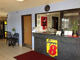 Una recepción con un letrero de 'Super 8', un reloj y una pared roja con una puerta.