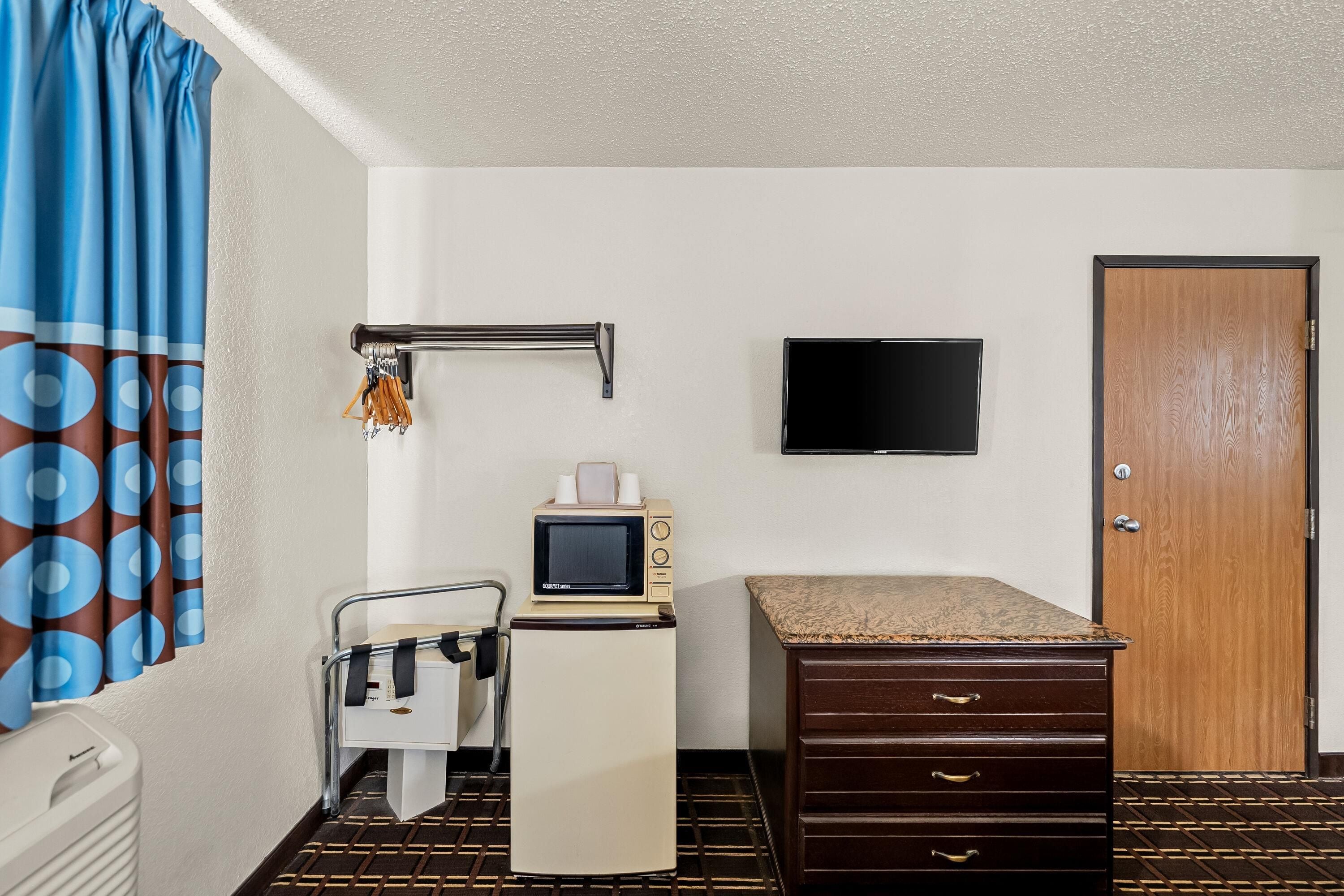A hotel room with a bed, a desk with a microwave, a TV, a wardrobe, and a bathroom with a towel rack.