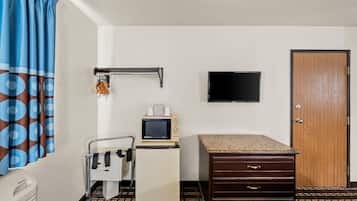 A hotel room with a bed, a desk with a microwave, a TV, a wardrobe, and a bathroom with a towel rack.