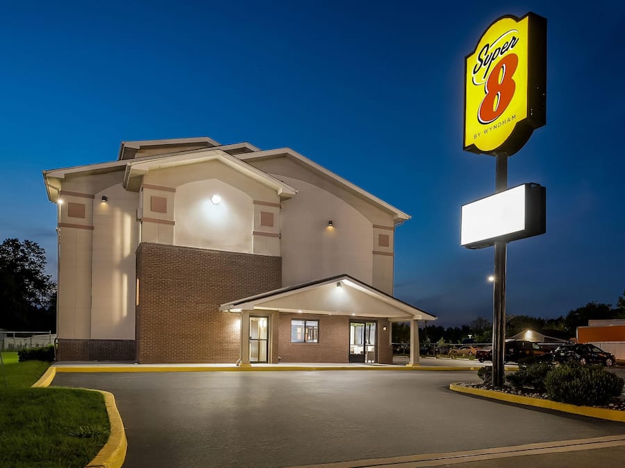 Um hotel Super 8 com fachada de tijolos, entrada coberta e um grande letreiro iluminado.