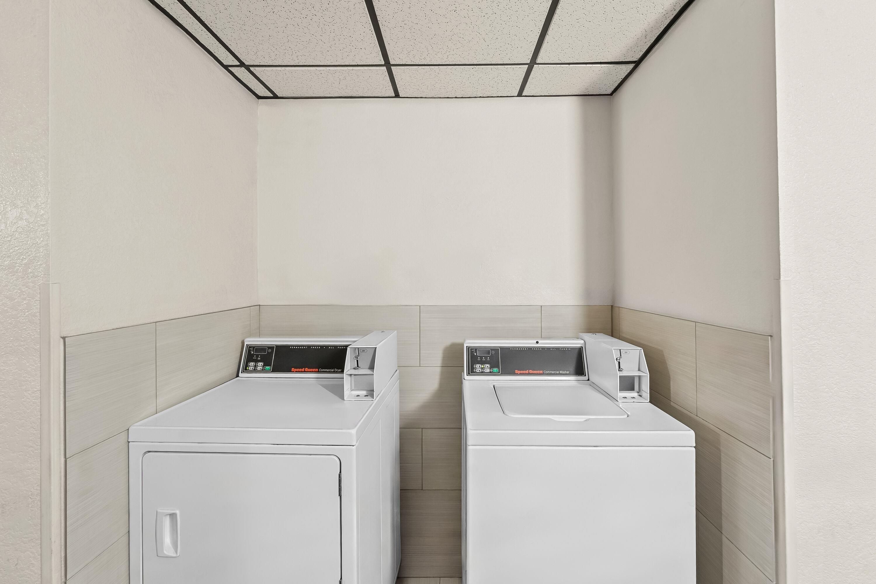 A laundry room with two white front-loading washers and dryers, a tiled ceiling, and light-colored walls.