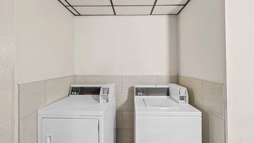 A laundry room with two white front-loading washers and dryers, a tiled ceiling, and light-colored walls.