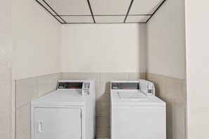 A laundry room with two white front-loading washers and dryers, a tiled ceiling, and light-colored walls. - Super 8 by Wyndham New Castle (New Castle)