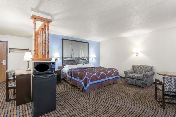 Habitación de hotel con cama, escritorio con microondas, silla, lámpara y alfombra estampada.