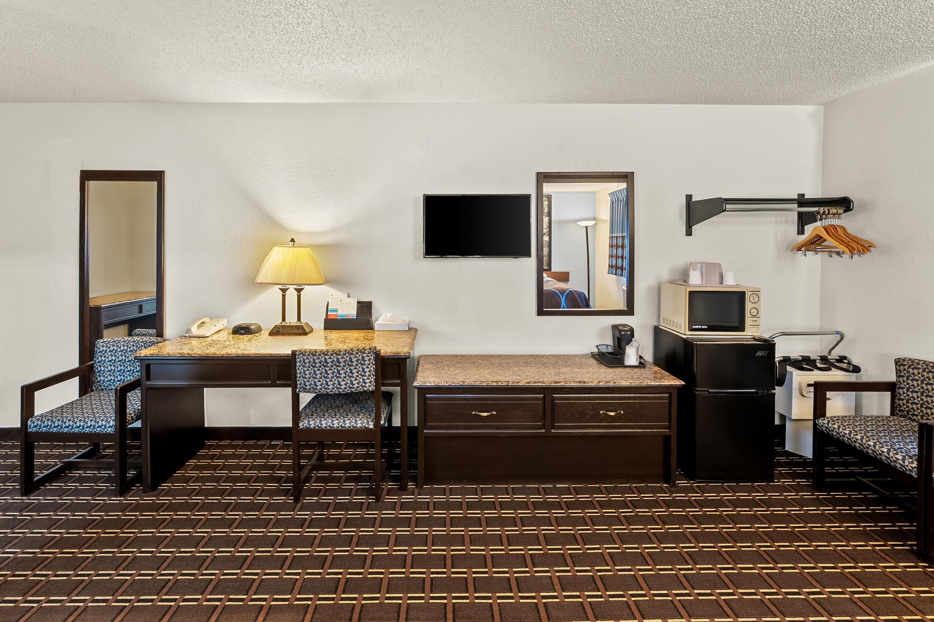 Habitación de hotel con escritorio, sillas, televisor, microondas y refrigerador pequeño.