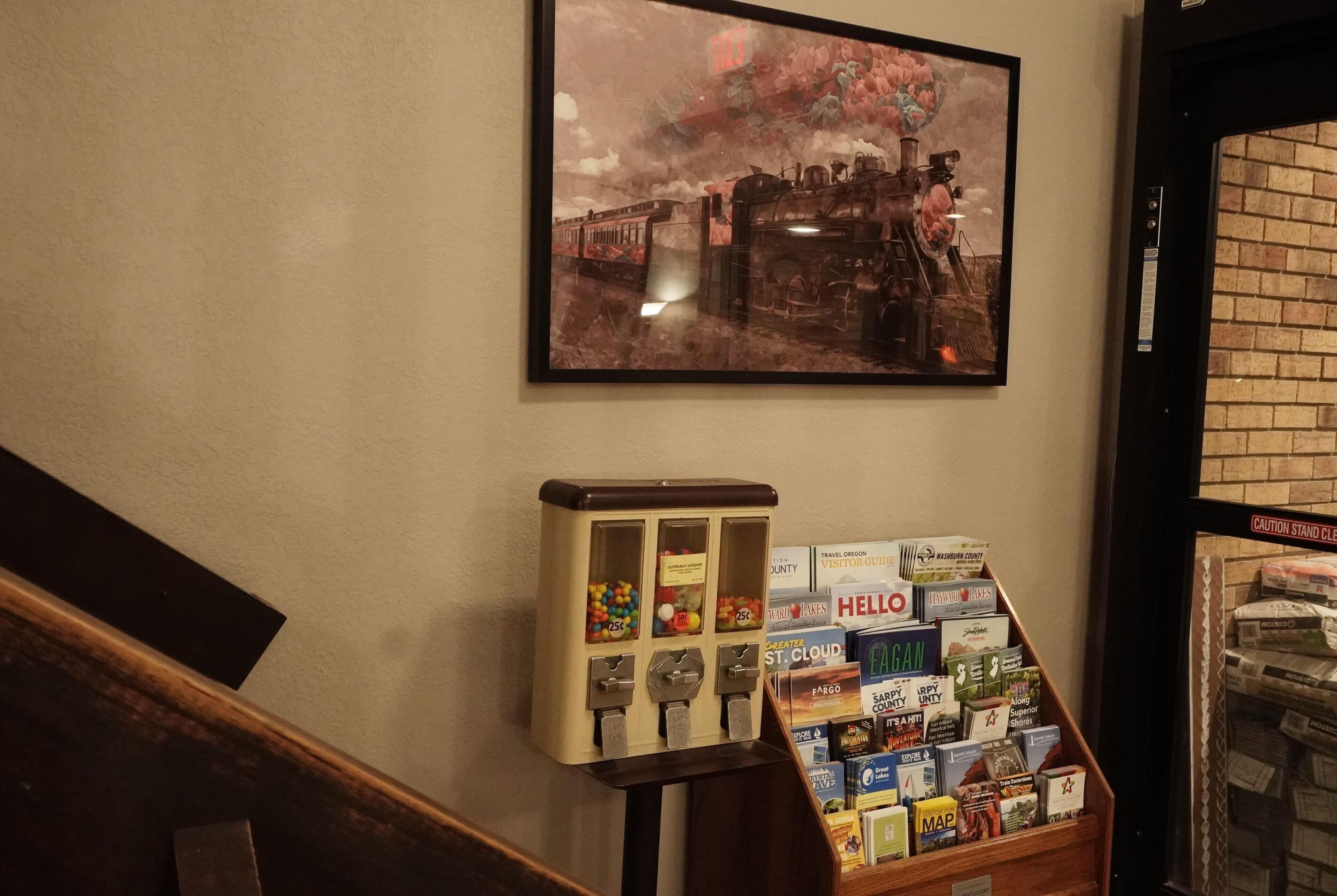 A wall-mounted painting of a train, a vintage-style vending machine, and a display of travel guides and maps.