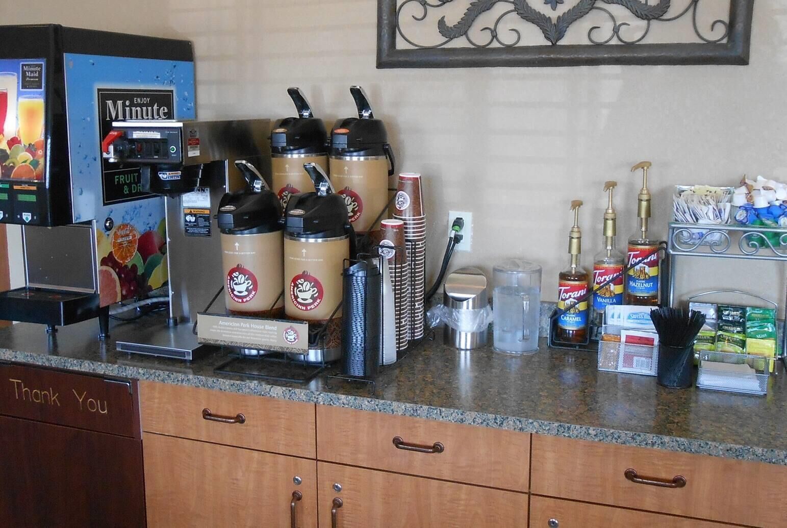 A coffee station with a coffee machine, multiple coffee dispensers, and a variety of condiments and beverages.