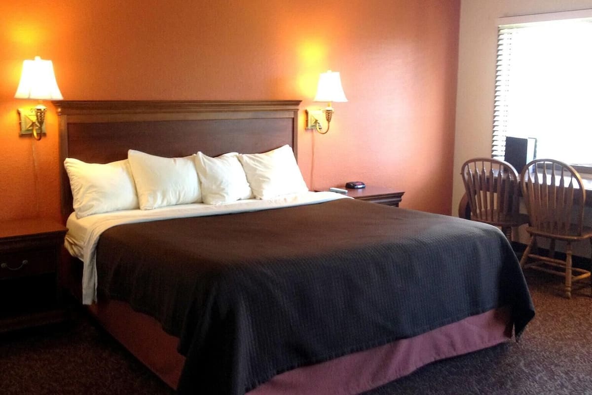 A hotel room with a bed, two bedside lamps, a nightstand, a chair, and a window with blinds.
