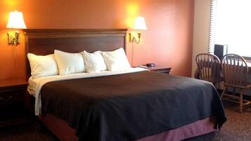 Una habitación de hotel con una cama, dos lámparas de noche, una mesita de noche, una silla y una ventana con persianas.
