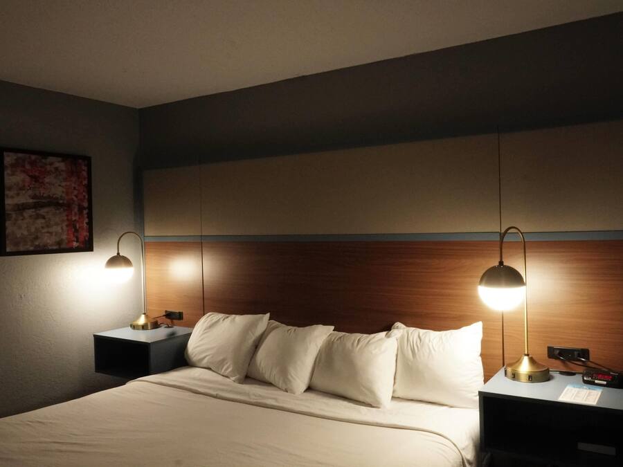 A hotel room with a bed, two bedside tables, a nightstand, a lamp, and a wall-mounted artwork.