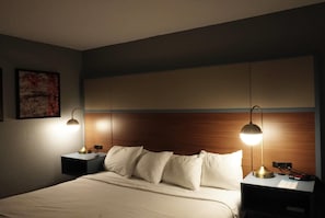 A hotel room with a bed, two bedside tables, a nightstand, a lamp, and a wall-mounted artwork.