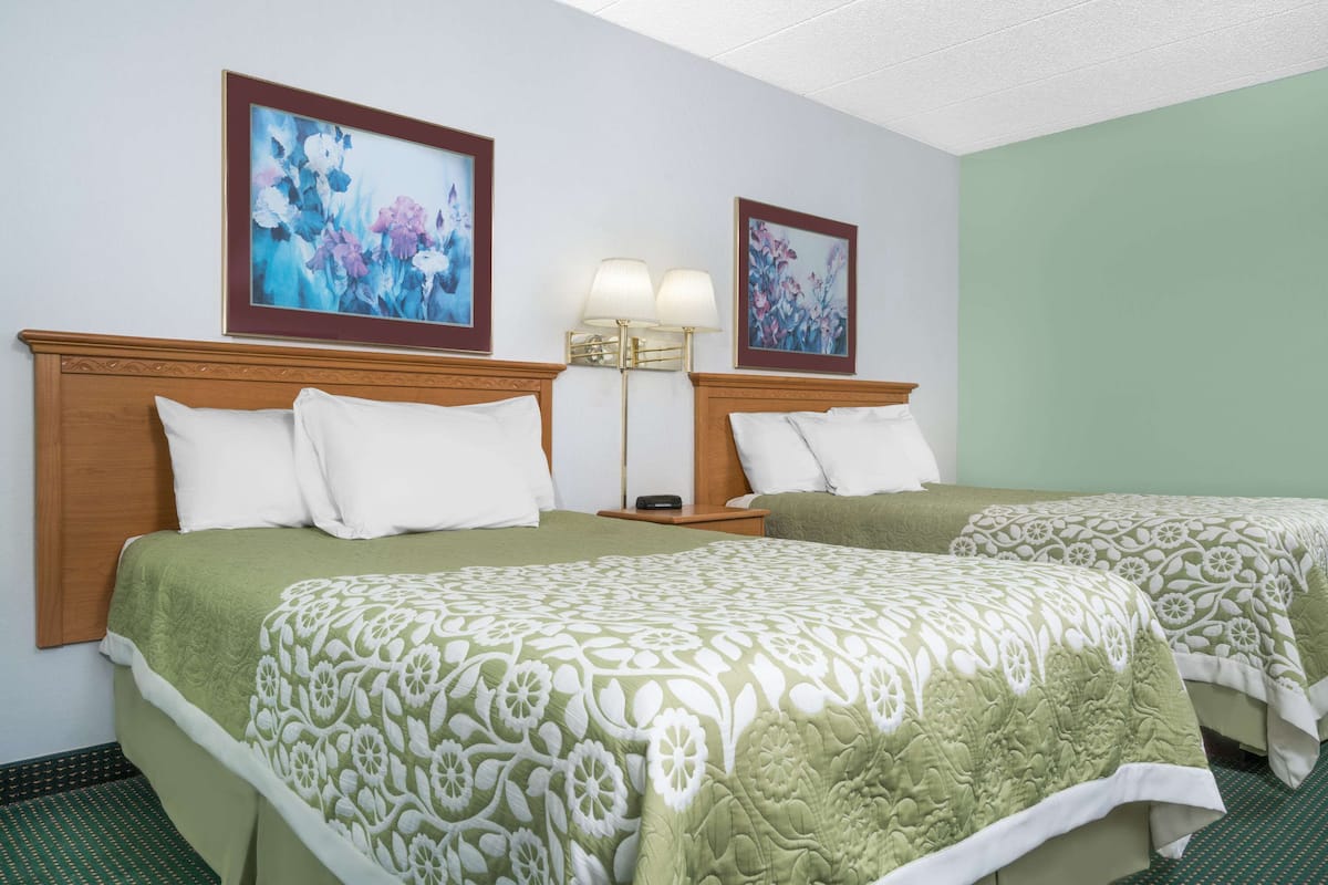 A hotel room with two beds, each with a green and white floral bedspread, a wooden headboard, and a nightstand with a lamp.