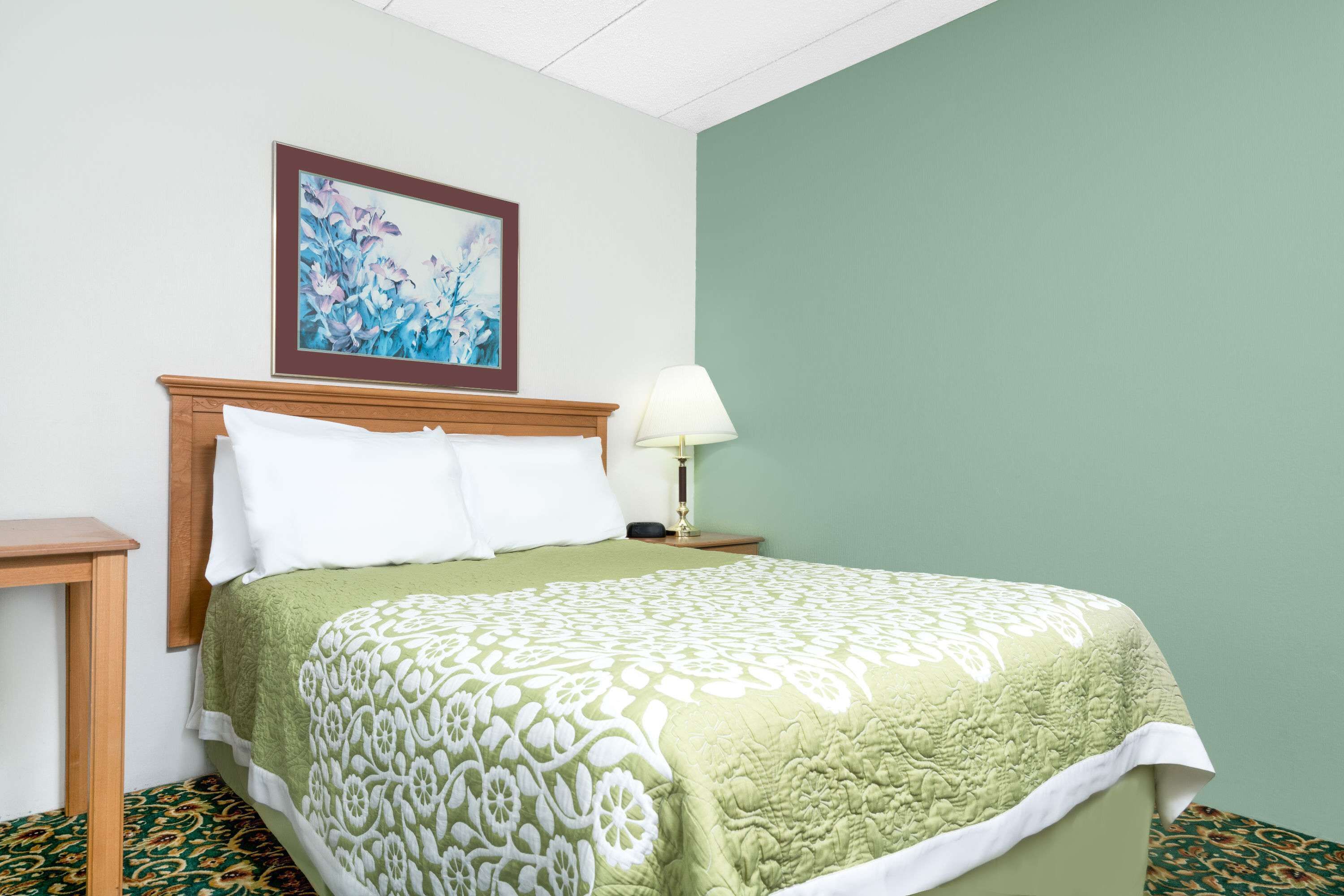 A hotel room with a bed, a nightstand, a lamp, and a framed floral artwork on the wall.
