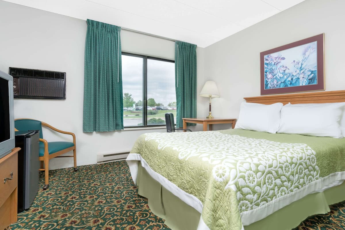 A hotel room with a bed, a desk, a chair, a television, and a window with curtains.