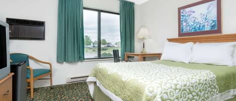Habitación de hotel con cama, escritorio, silla, televisor y ventana con cortinas.