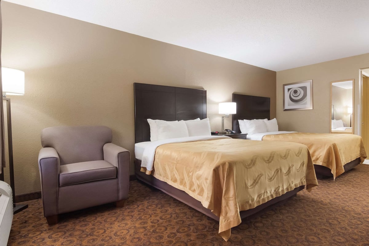 A hotel room with two beds, a chair, and a lamp.