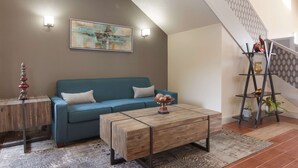 A living room with a blue sofa, a wooden coffee table, and a staircase with a patterned railing.