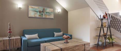 A living room with a blue sofa, a wooden coffee table, and a staircase with a patterned railing.