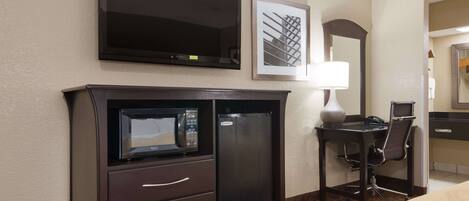 A hotel room with a flat-screen TV, a microwave, a desk with a chair, and a bed.