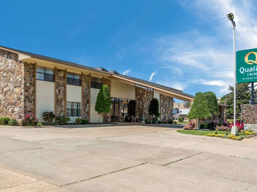 A Quality Inn by Choice Hotels with a stone facade, large windows, and a clear sky.
