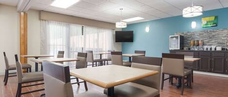 A dining area with tables and chairs, a kitchen area with a counter and appliances, and a television mounted on the wall.