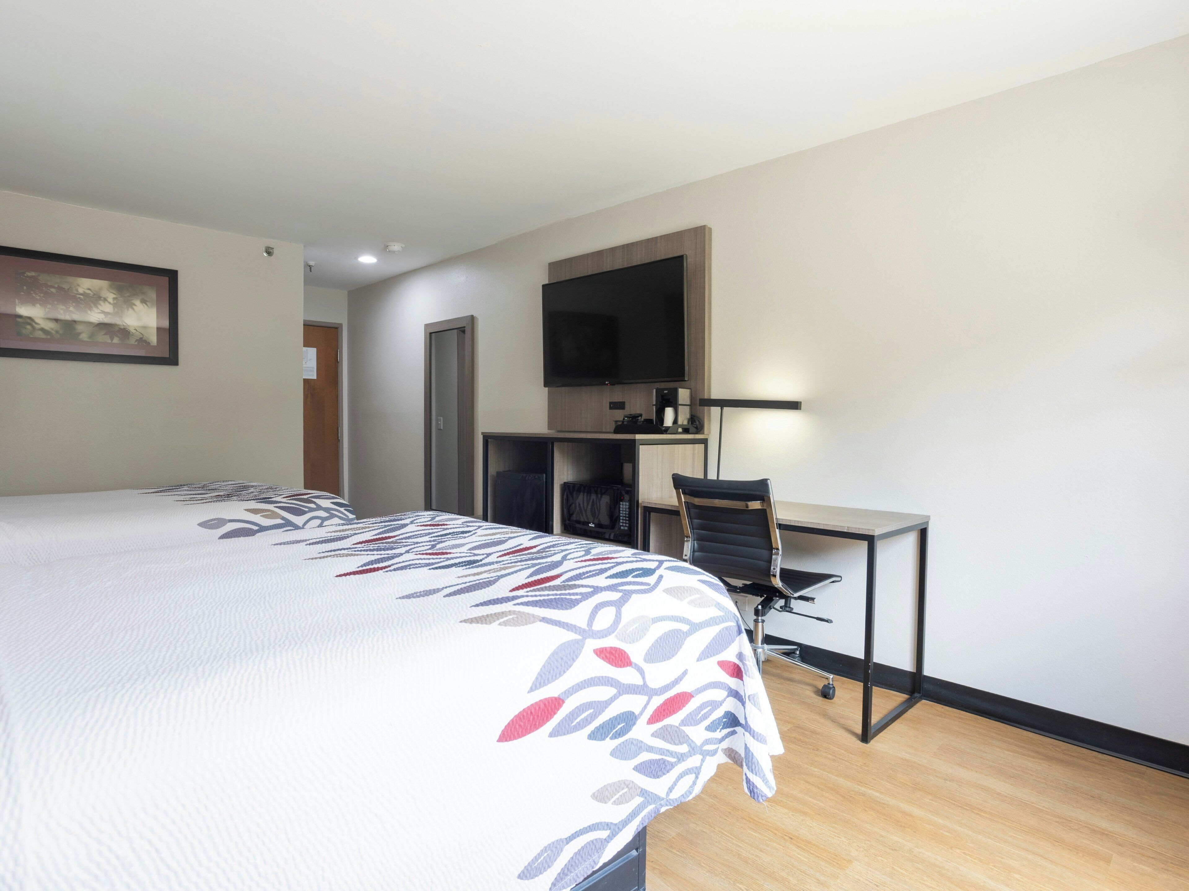 A hotel room with a bed, a desk, a chair, a television, and a door.