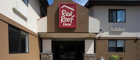 A Red Roof Inn building with a prominent red sign, stone pillars, and a parking lot.