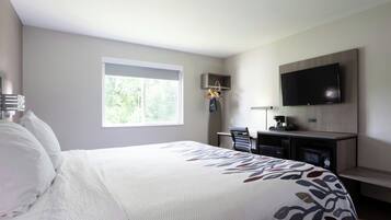 A hotel room with a large bed, a desk, a chair, a television, and a window with a view of trees.