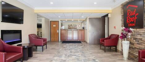 A hotel lobby with a reception desk, seating area, and a TV screen.