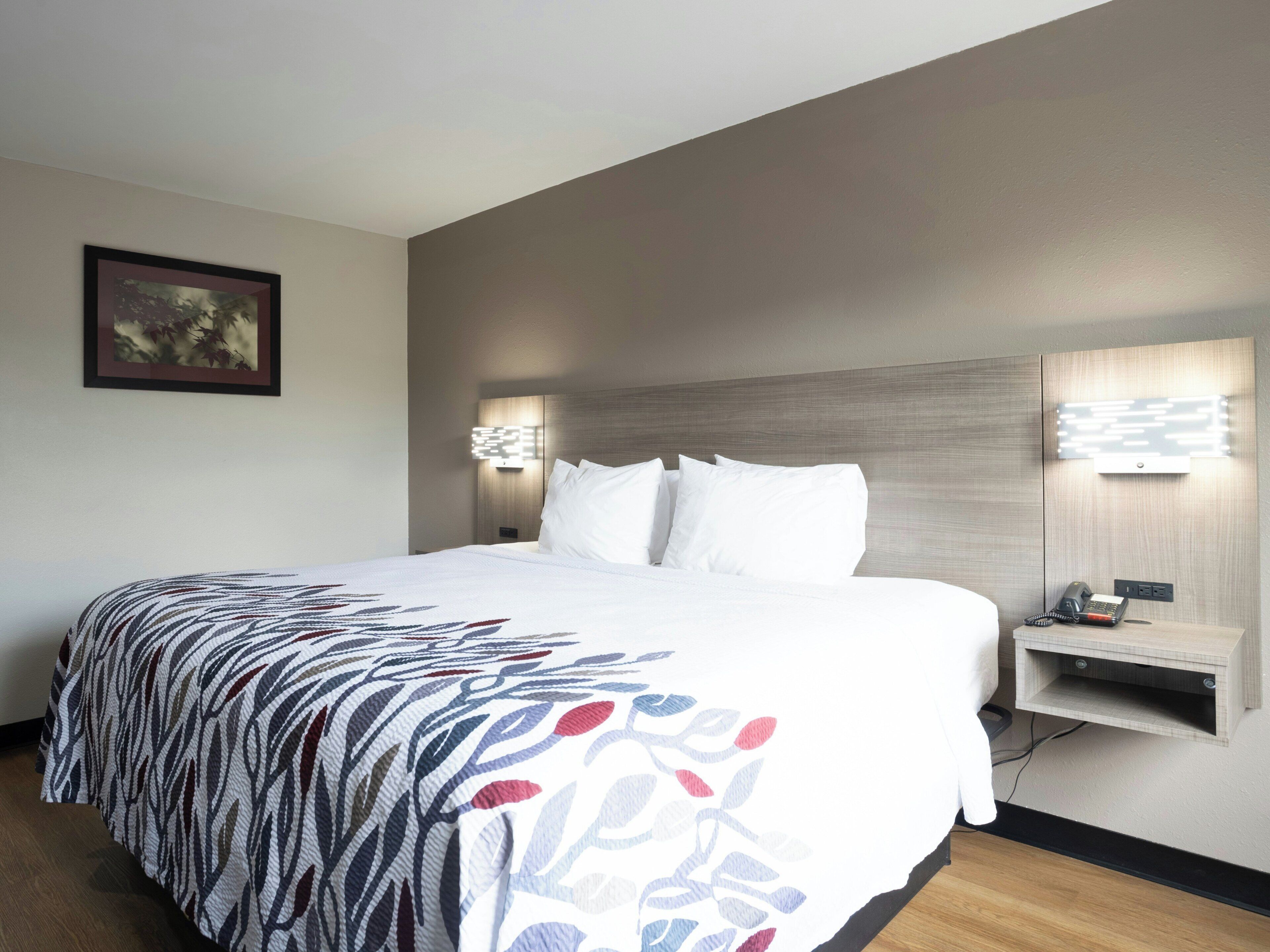 A hotel room with a large bed, a bedside table, a wall-mounted light, and a framed picture on the wall.