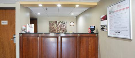 A reception desk with a clock, a framed informational poster, and a security camera above.