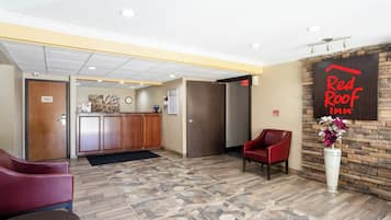 A hotel lobby with a reception desk, a red chair, a clock, and a Red Roof Inn sign.