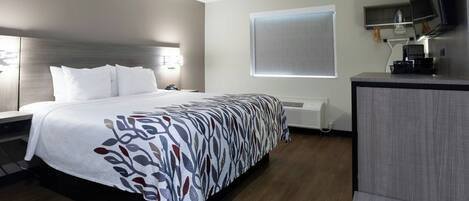 A hotel room with a bed, bedside table, wall-mounted TV, and a window with blinds.