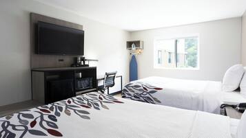 A hotel room with two beds, a TV, a desk with a coffee maker, and a window with a view.