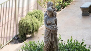 A statue of a woman holding a bunch of grapes, surrounded by greenery and a metal fence. - California Inn (Barstow)