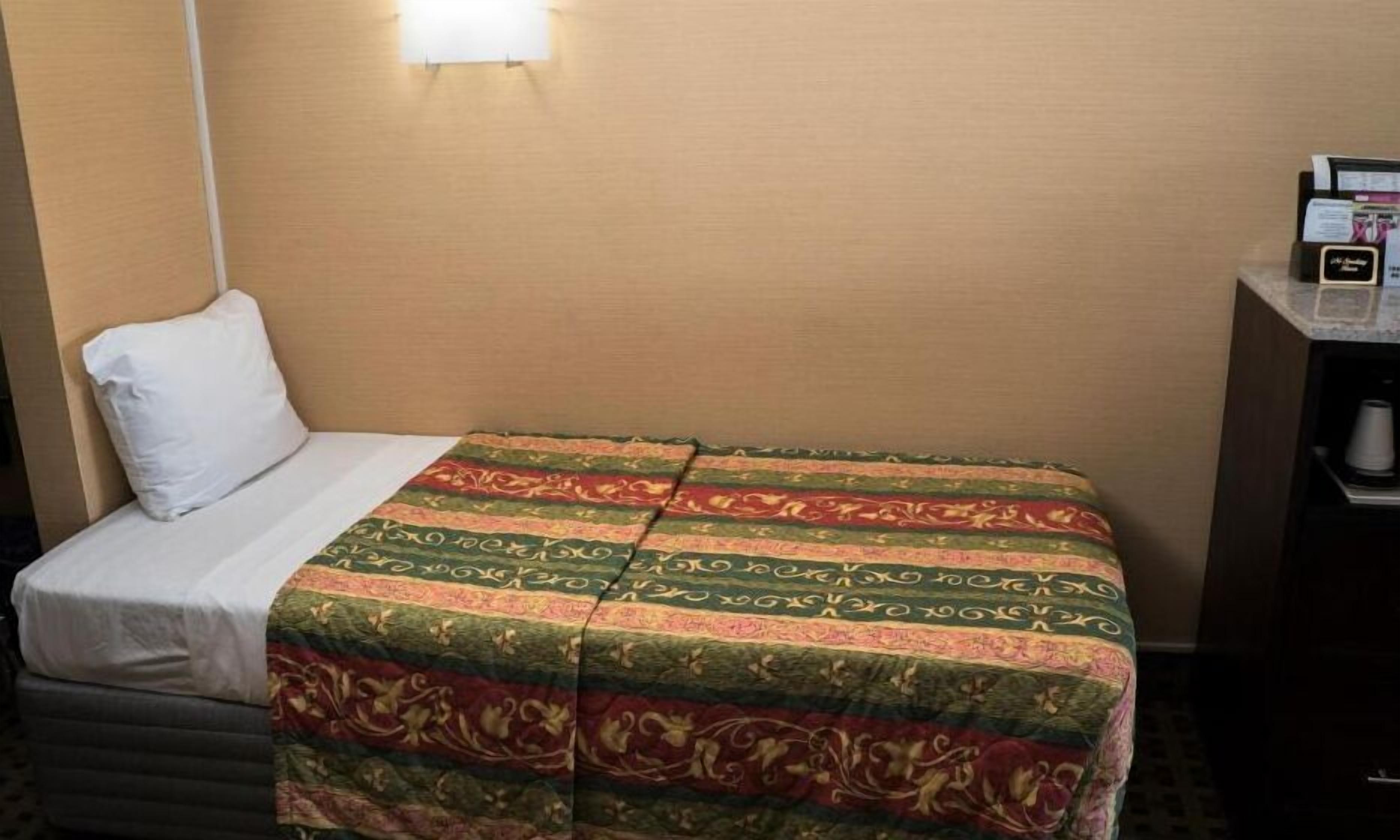 A hotel room with a bed, a white pillow, a patterned bedspread, a nightstand with a phone, and a coffee maker.