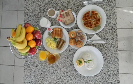 A breakfast spread on a granite countertop including fruits, toast, waffles, eggs, and pastries.