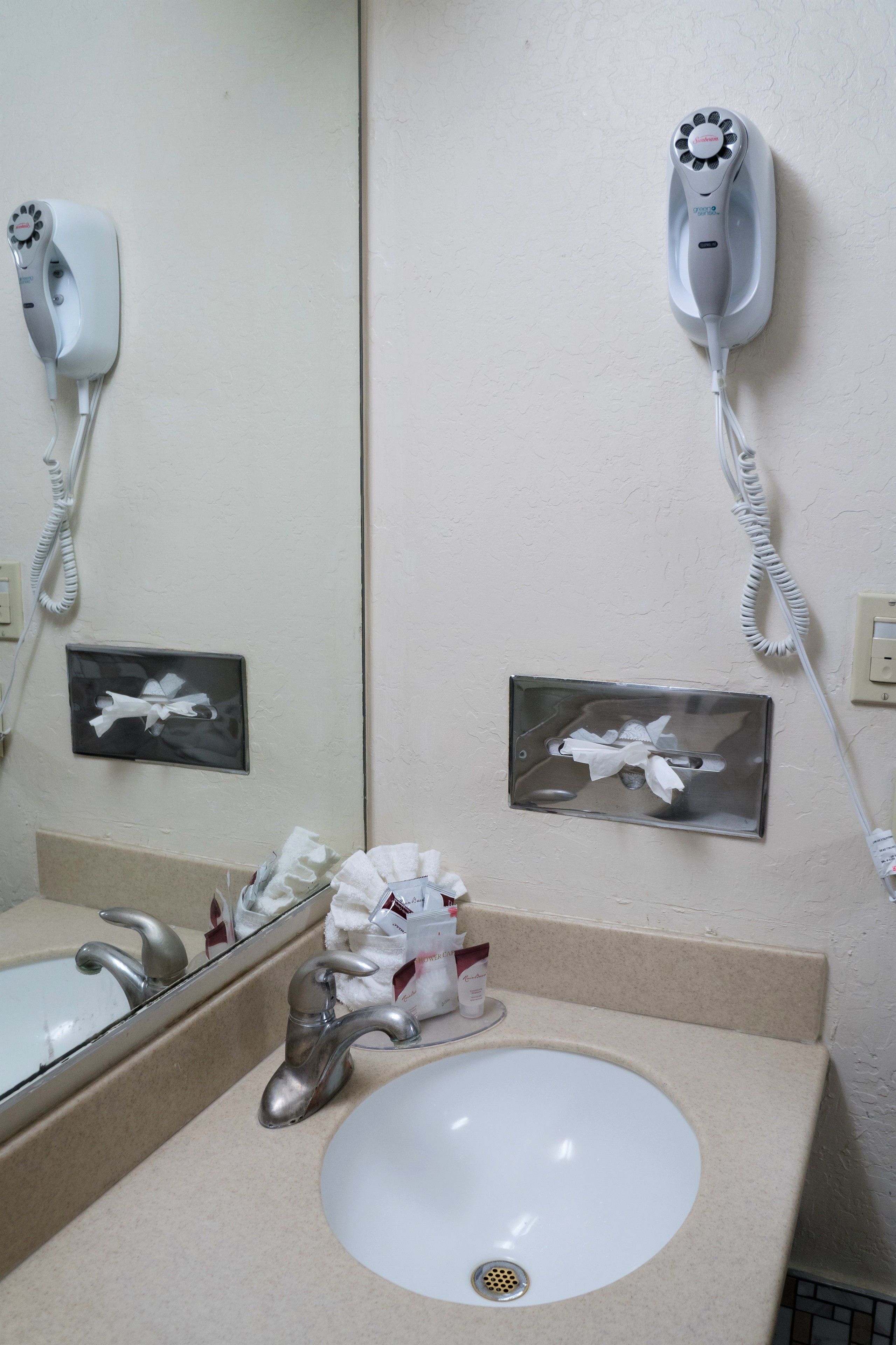 A bathroom with a sink, mirror, and two hair dryers mounted on the wall.
