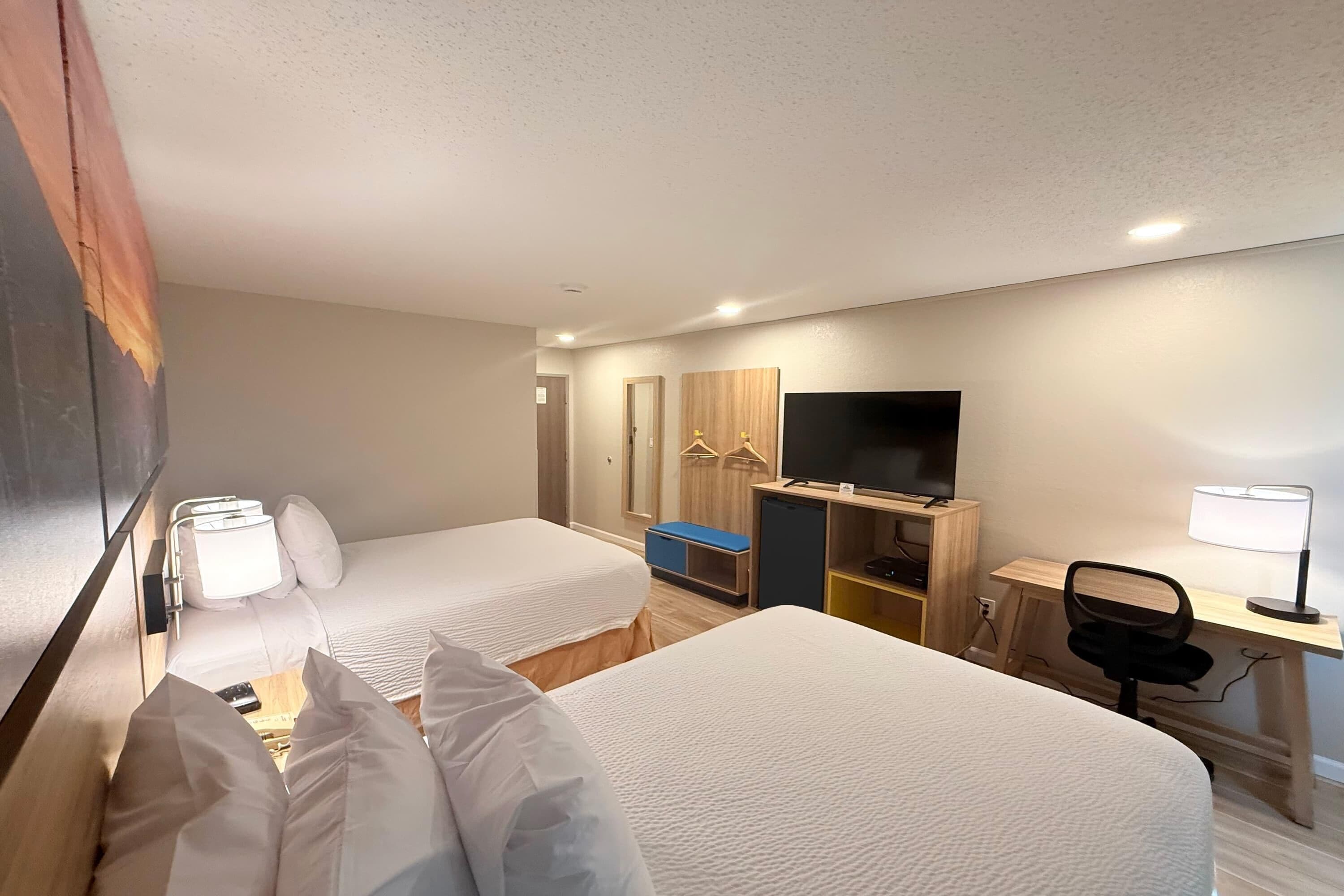 A hotel room with two beds, a desk with a chair, a TV, and a wardrobe.