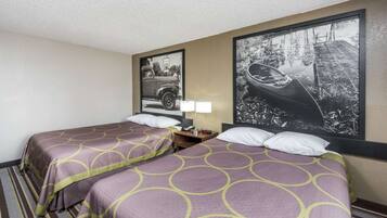 A hotel room with two beds, a nightstand, a lamp, and two framed pictures on the wall.