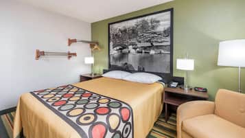Une chambre d’hôtel avec un lit, une chaise, un bureau avec une lampe, un téléphone et un tableau au mur.