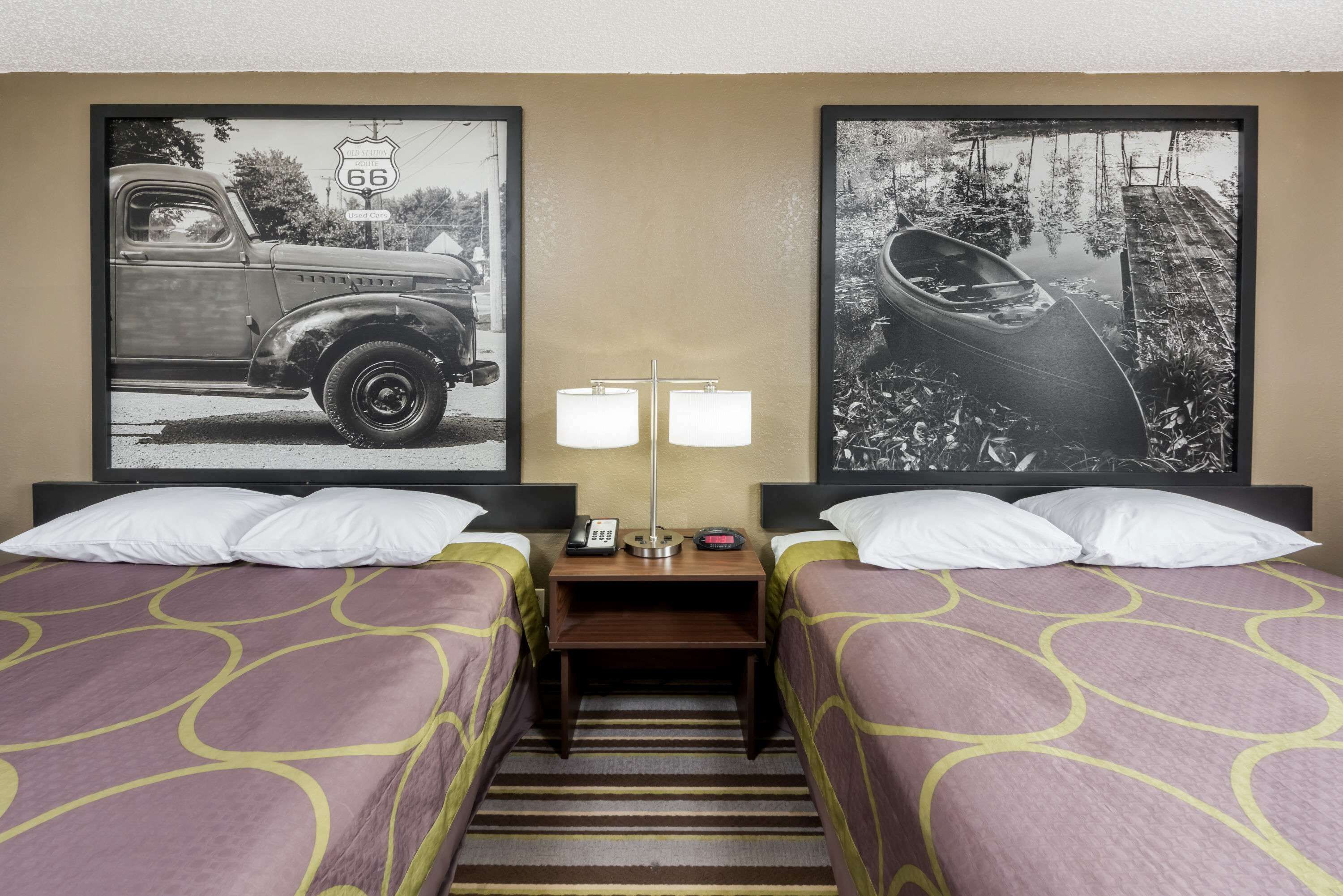 A hotel room with two beds, a nightstand with a lamp, and two framed pictures on the wall.