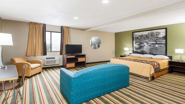 A hotel room with a bed, a sofa, a TV, a desk with a chair, and a window with curtains. - Super 8 by Wyndham Bloomington/Normal (Bloomington)