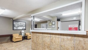 A reception area with a marble counter, two armchairs, a framed welcome sign, and a 'Come Stay with Us' sign. - Super 8 by Wyndham Bloomington/Normal (Bloomington)