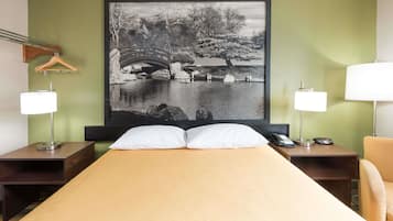 A hotel room with a bed, two bedside tables with lamps, a hanging coat rack, and a large black and white photograph on the wall.