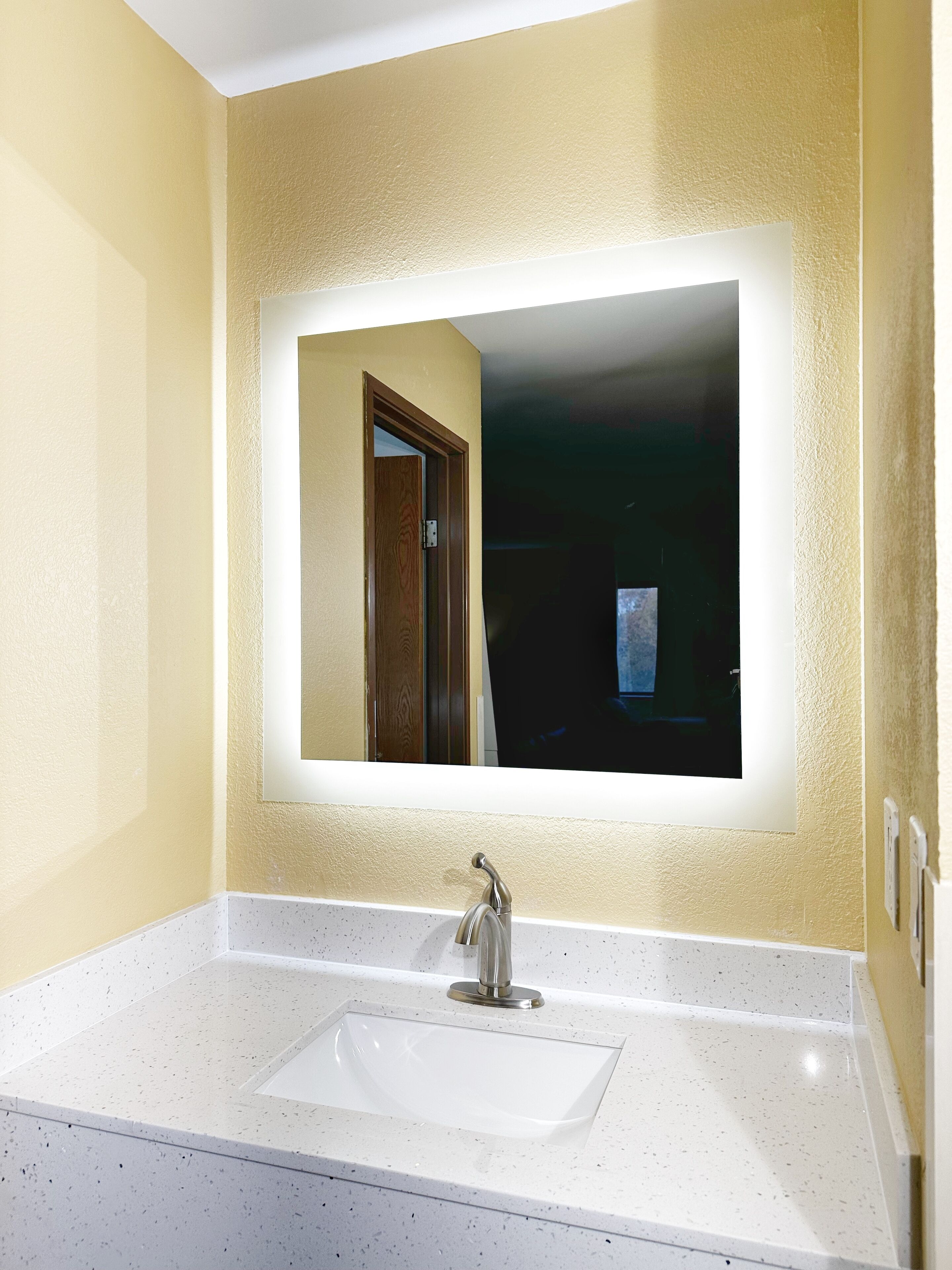 Un baño con un lavamanos blanco, un espejo con luz y una puerta.
