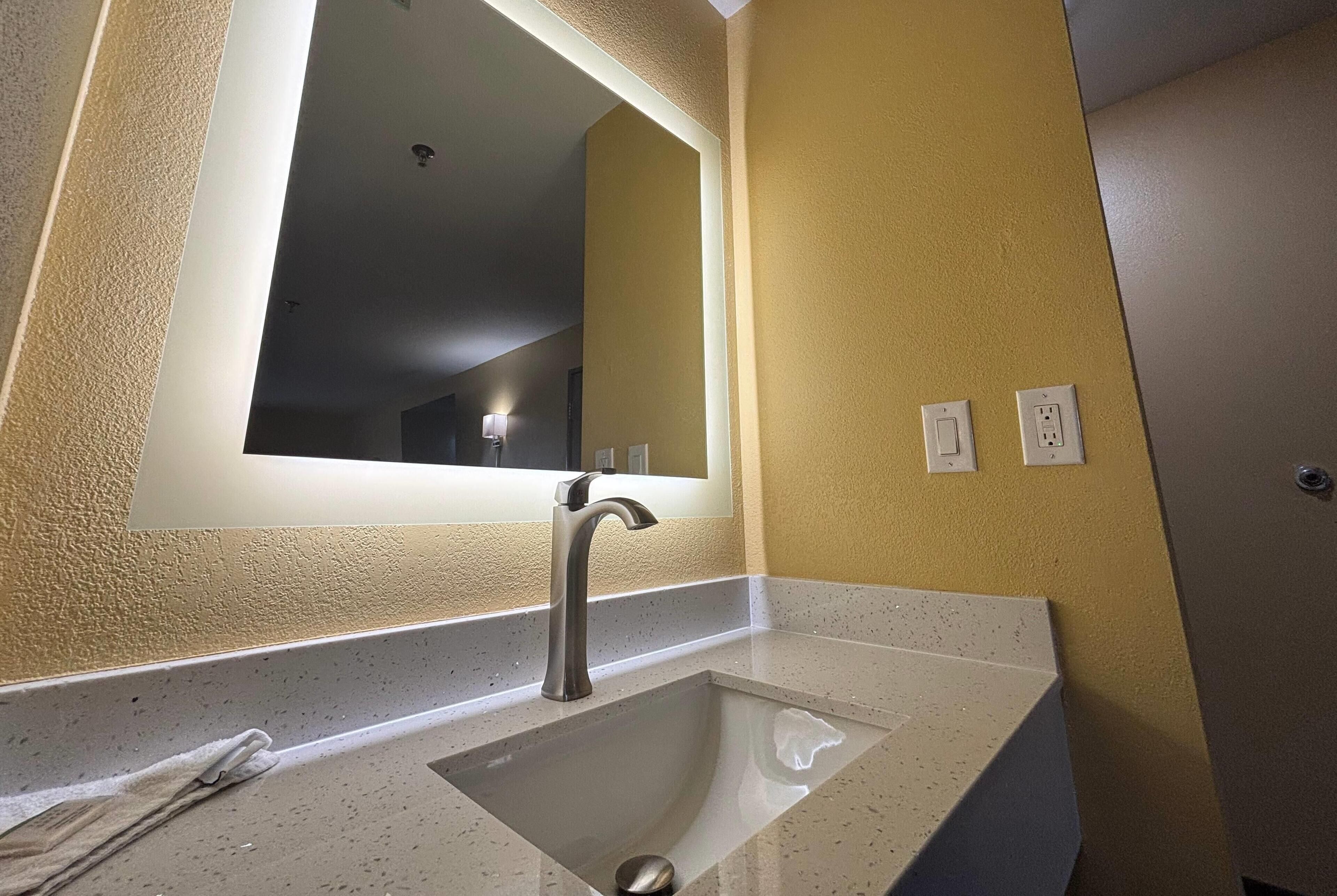Un baño con lavamanos, espejo y dos enchufes en la pared.