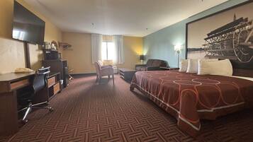 A hotel room with a large bed, a desk with a chair, a TV, and a window with curtains.