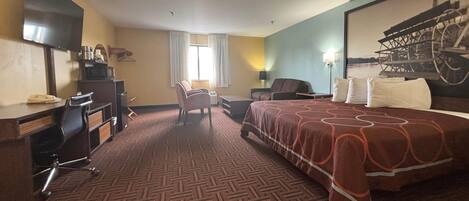 Habitación de hotel con una cama grande, un escritorio con silla, televisión y ventana con cortinas.