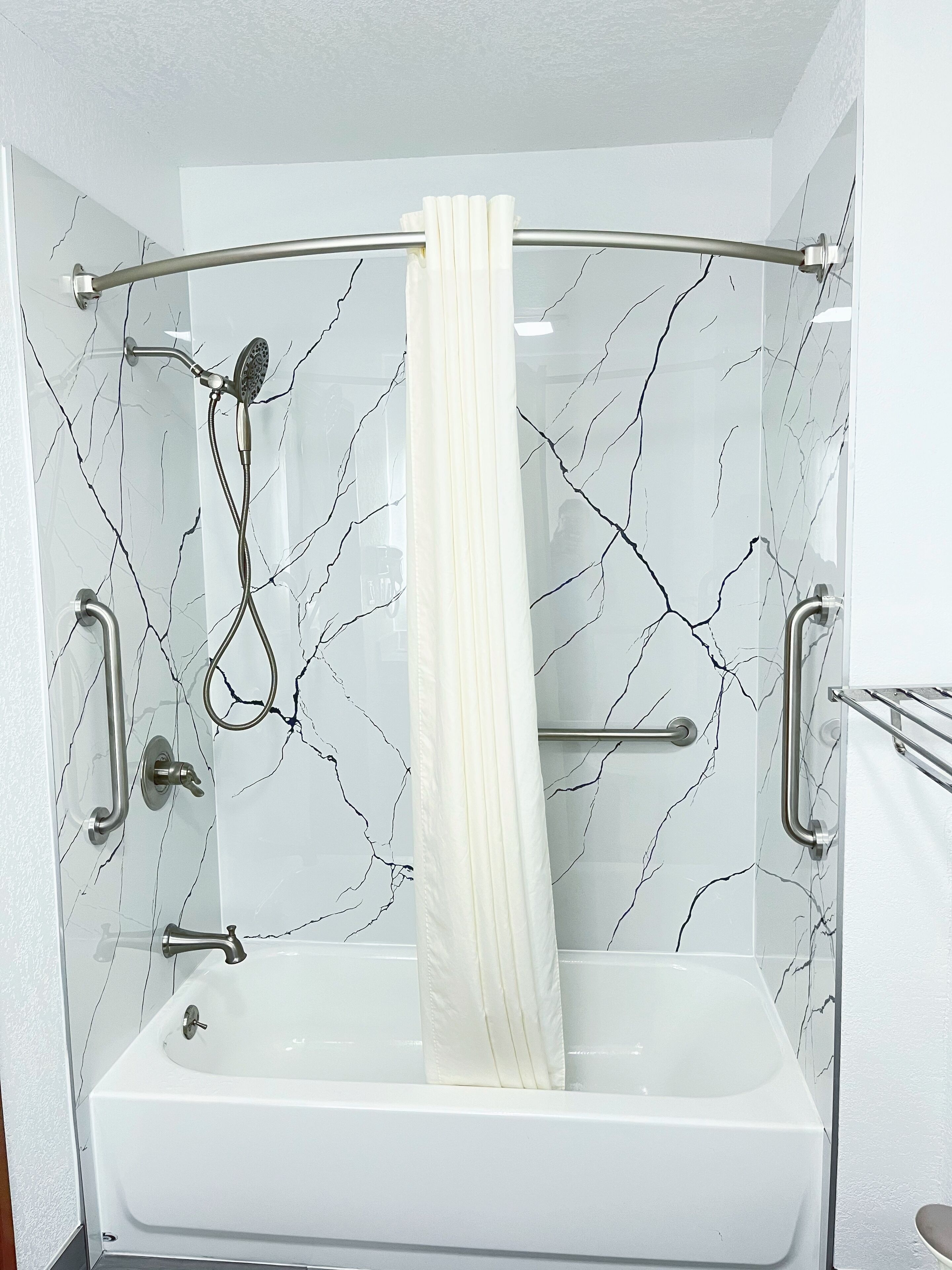 Un baño moderno con ducha envuelta en cristal, una bañera blanca y paredes con diseño de mármol.